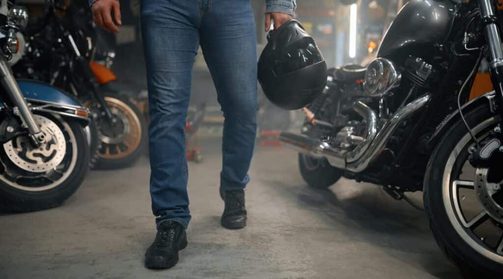 Mann mit Motorradhelm steht zwischen gebrauchten Motorrädern in einer Werkstatt – Symbolbild für Motorrad Occasion.